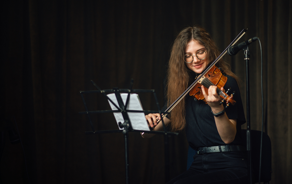 A student violinist rehearses confidently on stage, reading sheet music and performing under soft lighting.
