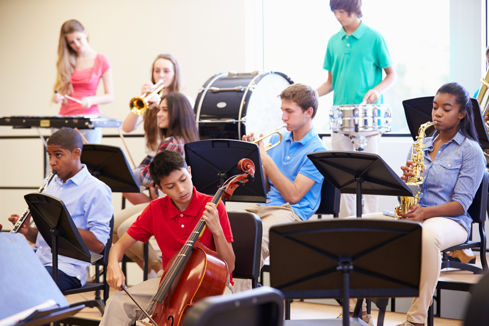 A diverse group of middle and high school students rehearses together in a school band, playing a variety of orchestral and percussion instruments.