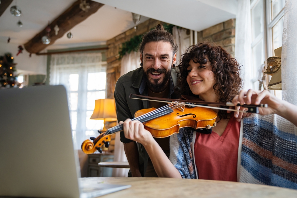 Violin,Teacher,Helping,A,Woman,Student,At,Home An adult student and instructor share a joyful moment during a violin lesson at home.