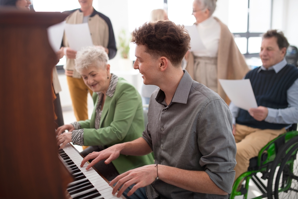 Young man playing piano with elderly woman, smiling