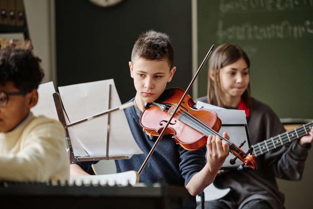 Middle school aged boy focusing on sheet music while playing violin in music class
