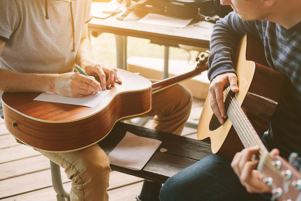 Learning,To,Play,The,Guitar.,Music,Education,And,Extra-curricular,Lessons. Two guitar students collaborate on songwriting, jotting down notes while practicing together during a music lesson.