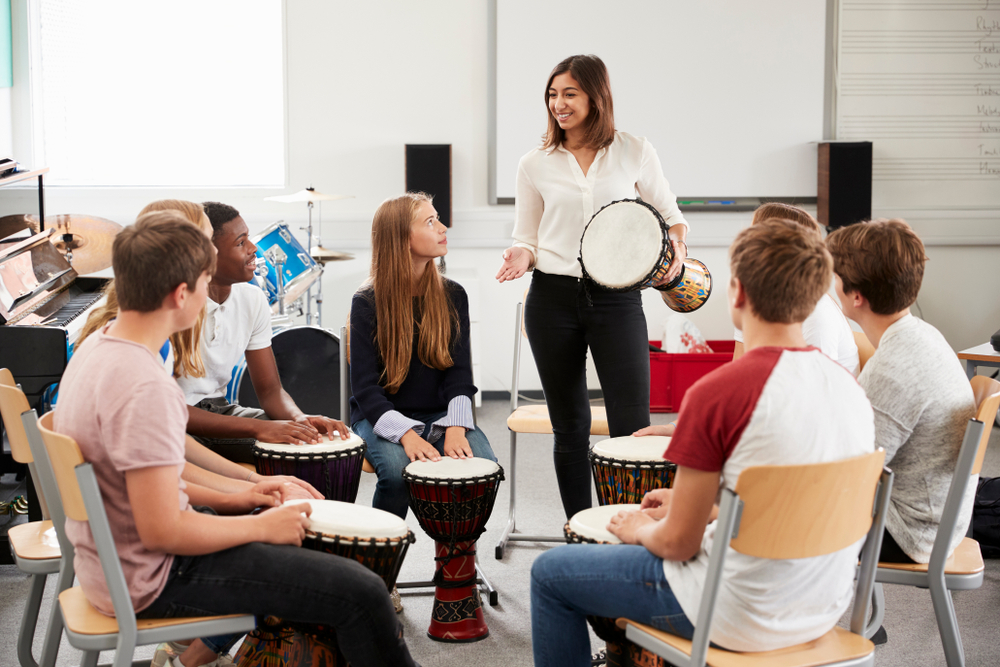 Teenage,Students,Studying,Percussion,In,Music,Class A music teacher leads a group of students in a rhythm-based drumming activity during a classroom percussion lesson.